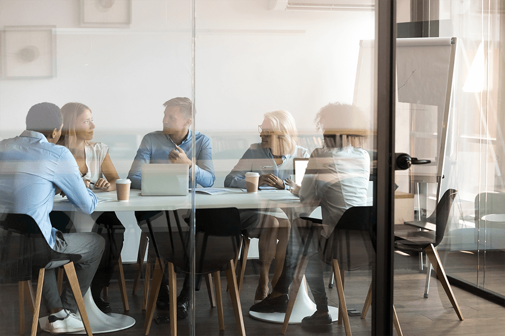 Three coworkers discussing plans written on a glass dry erase board